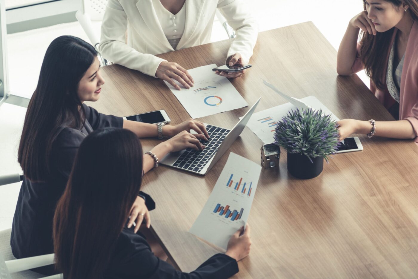 Businesswoman in group meeting discussion with other businesswomen colleagues in modern workplace office with laptop computer and documents on table. People corporate business working team concept.