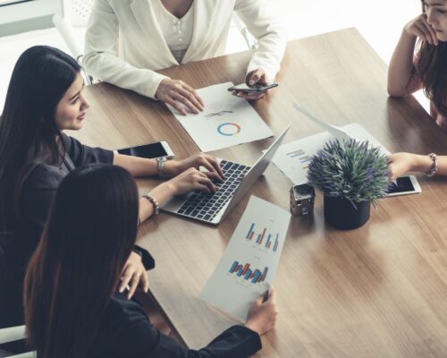 Businesswoman in group meeting discussion with other businesswomen colleagues in modern workplace office with laptop computer and documents on table. People corporate business working team concept.